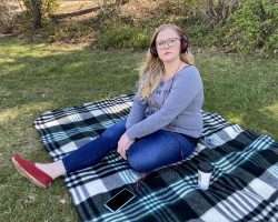 Woman seated on blanket outdoors, wearing headphones